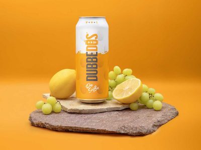 DUBBEDOS Süße Weinschorle-Dose, dekoriert mit einer frischen Zitrone und grünen Trauben vor einem leuchtenden orangefarbenen Hintergrund.