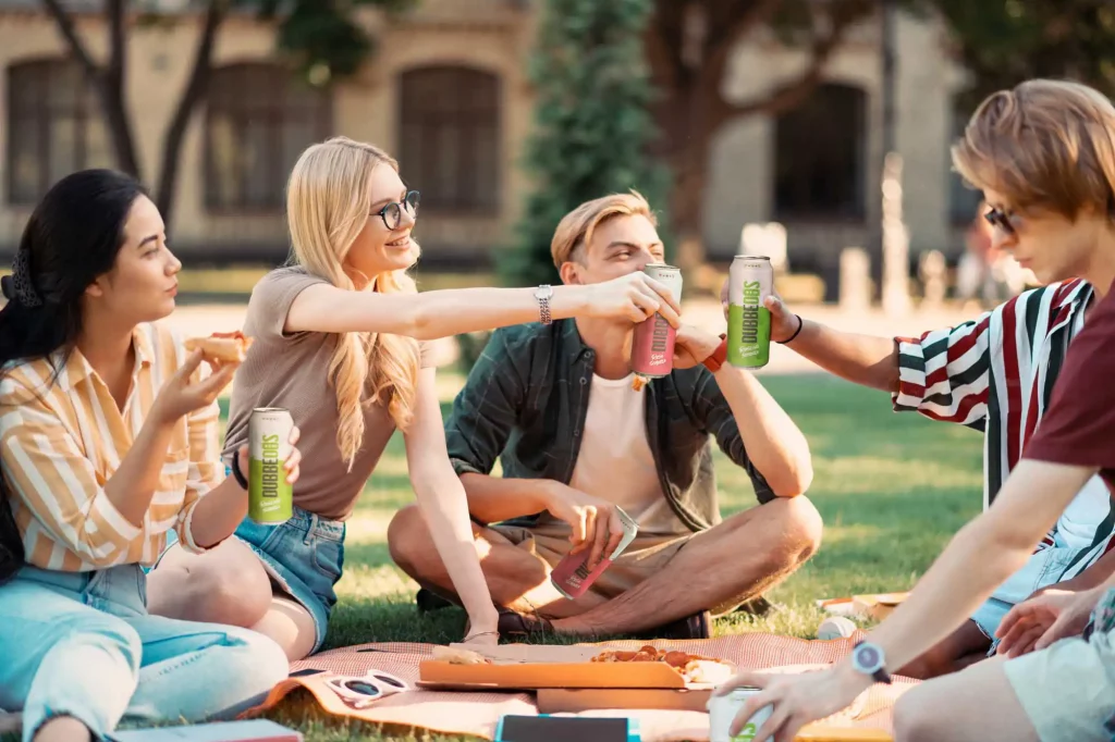 Vier Freunde stoßen bei einem Picknick im Park mit Dubbedos Weinschorle in der Dose an und genießen eine entspannte Zeit im Grünen.